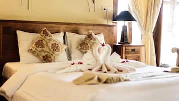 A neatly made bed with white linens and decorative pillows, a wooden headboard, and a bedside table with a lamp.
