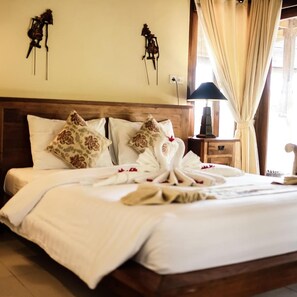 A neatly made bed with white linens and decorative pillows, a wooden headboard, and a bedside table with a lamp.