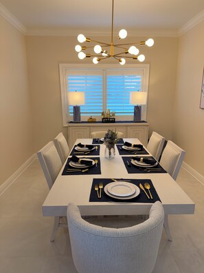A dining room with a white table set for six, featuring gold and white tableware, a vase with flowers, and a modern chandelier. - Snowbird Waterfront Retreat 3BR, Private 40' Dock, Heated Pool & Garage Like New (Punta Gorda)
