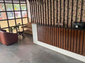Zona d'acollida amb un taulell de recepció de fusta, un sofà i una cadira.