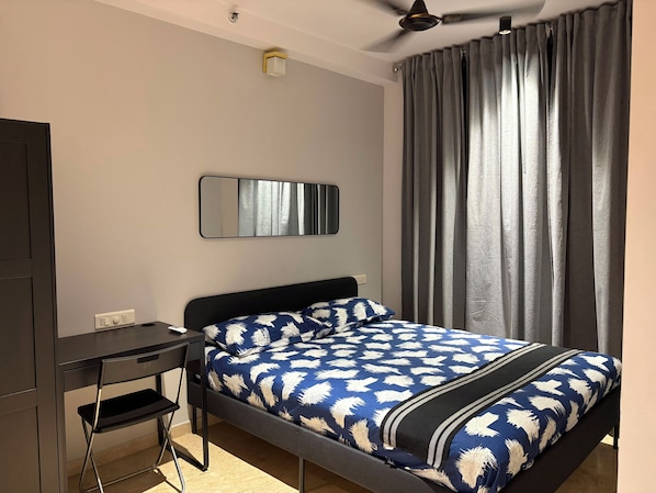 A bedroom with a bed, a desk, a chair, a ceiling fan, and a window with curtains.