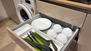 Una cocina equipada con lavadora, estufa y un cajón con platos y utensilios.