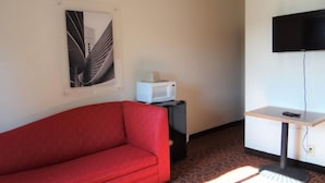 A room with a red sofa, a small table with a remote control, a white microwave, and a flat-screen TV mounted on the wall. - Bayshore Inn (Port Clinton)