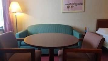 Une chambre d’hôtel avec une table ronde, deux fauteuils, un lit, une lampe et un tableau encadré au mur.