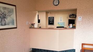 Un comptoir d’accueil avec une horloge au-dessus, une œuvre d’art encadrée accrochée au mur et un panneau d’information.