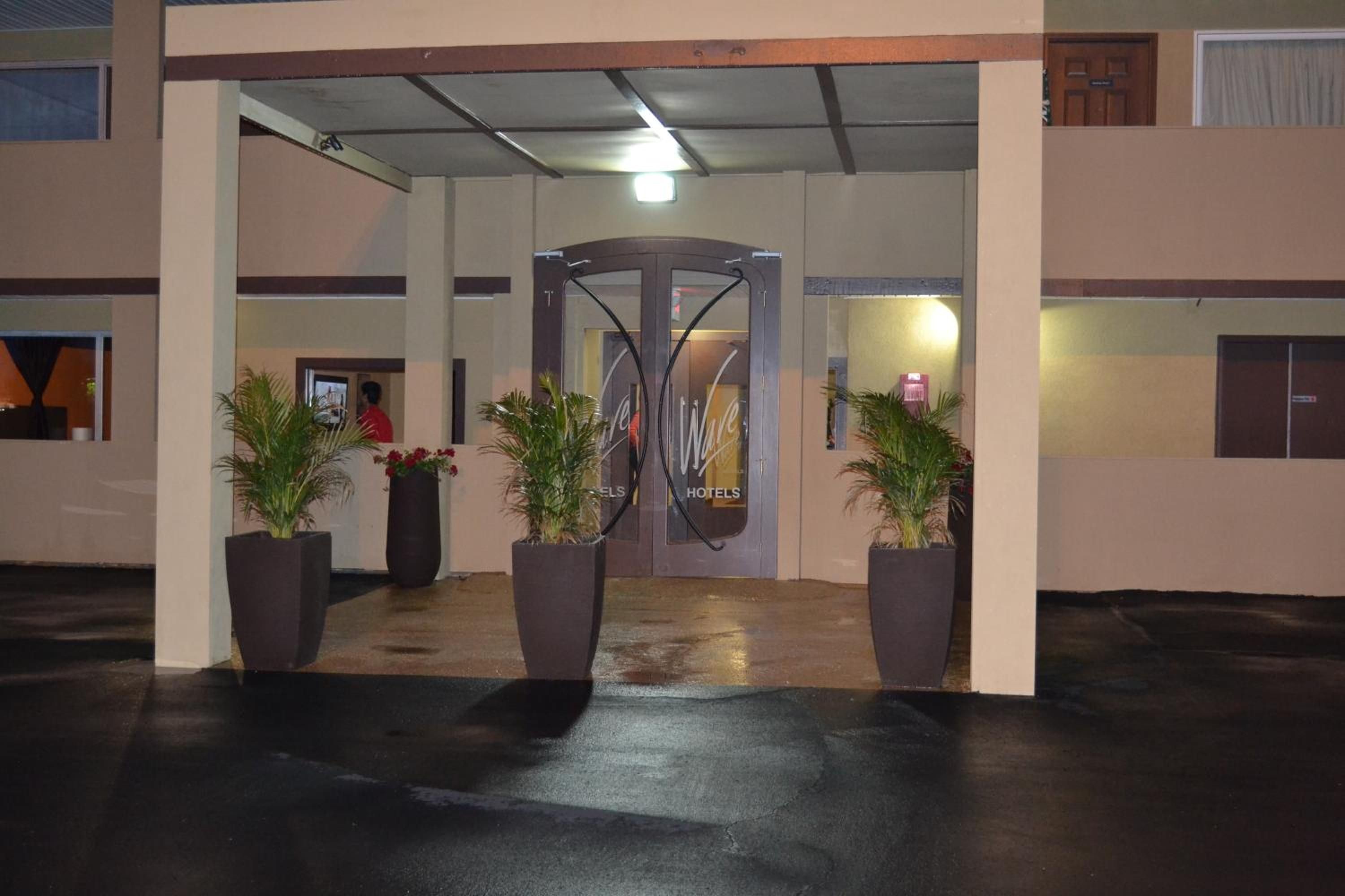 A hotel entrance with a glass door, potted plants, and a wet floor.