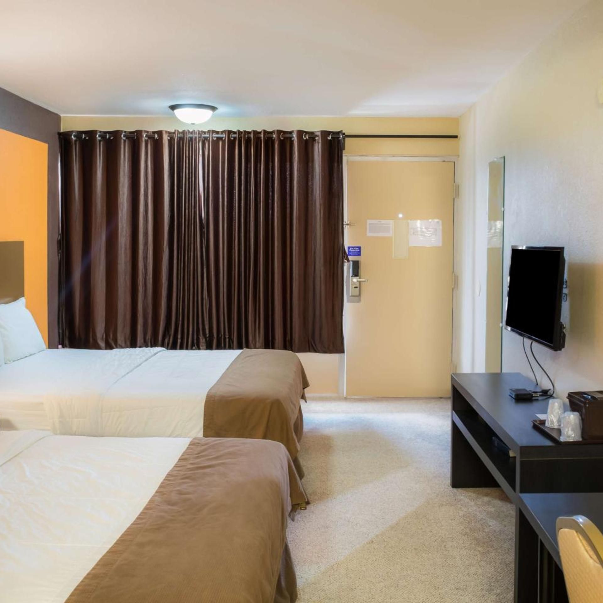 A hotel room with two beds, a desk with a television, and a door with a sign.