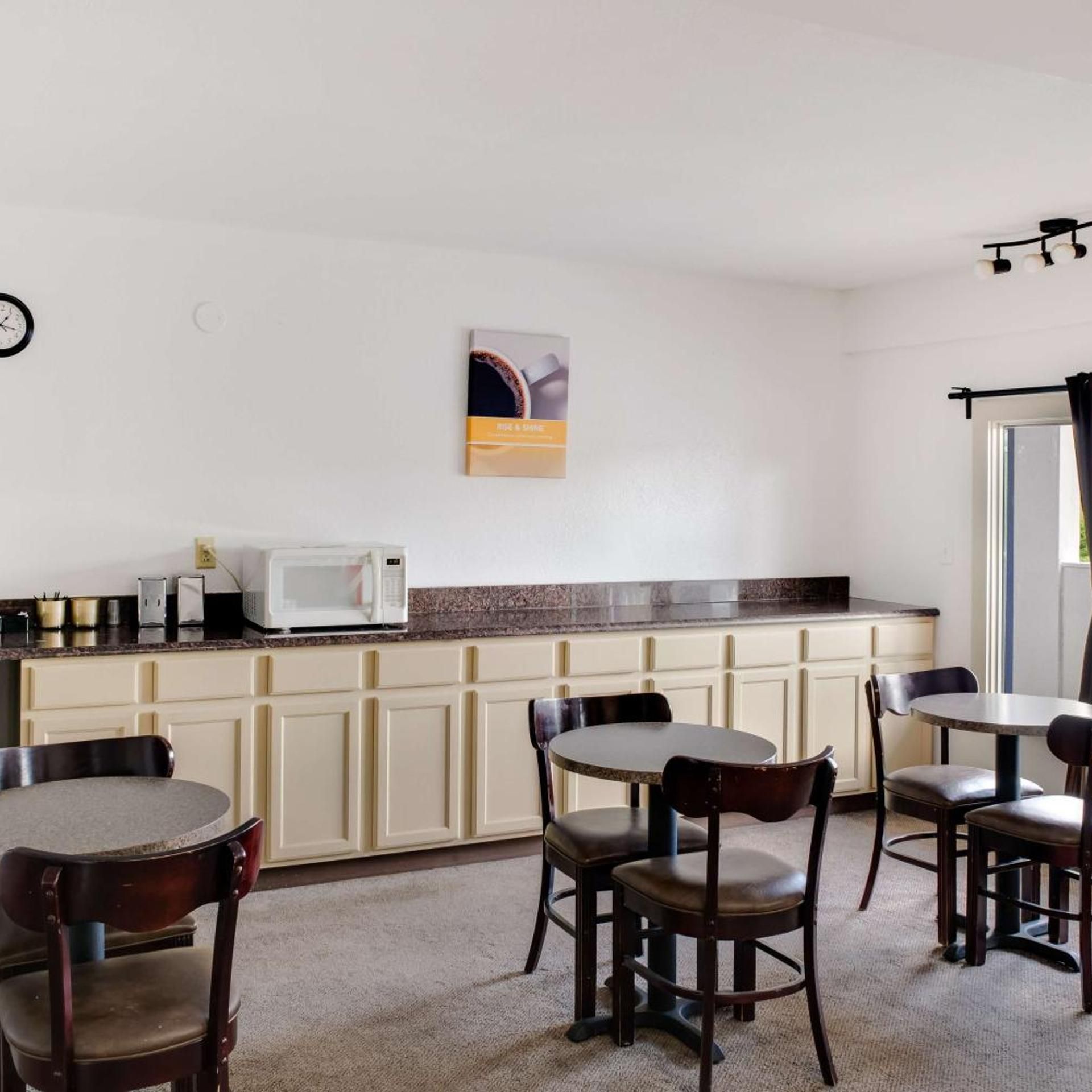 A kitchen with a microwave, cabinets, and a coffee machine. There are four chairs and a table.