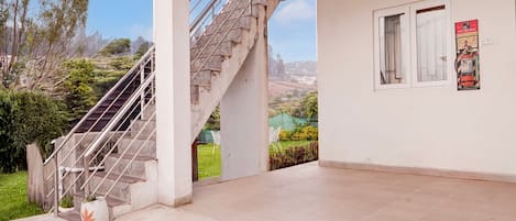 A building with a staircase leading to a balcony, a white wall with a poster, and a view of a green landscape.