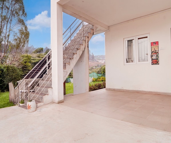 A building with a staircase leading to a balcony, a white wall with a poster, and a view of a green landscape.