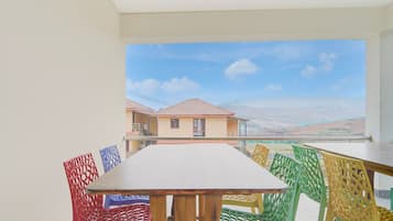 A balcony with a table and chairs, overlooking a residential area with houses and a clear sky.