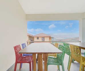 A balcony with a table and chairs, overlooking a residential area with houses and a clear sky. - Classic Aathira Hill Stay (Ootacamund)