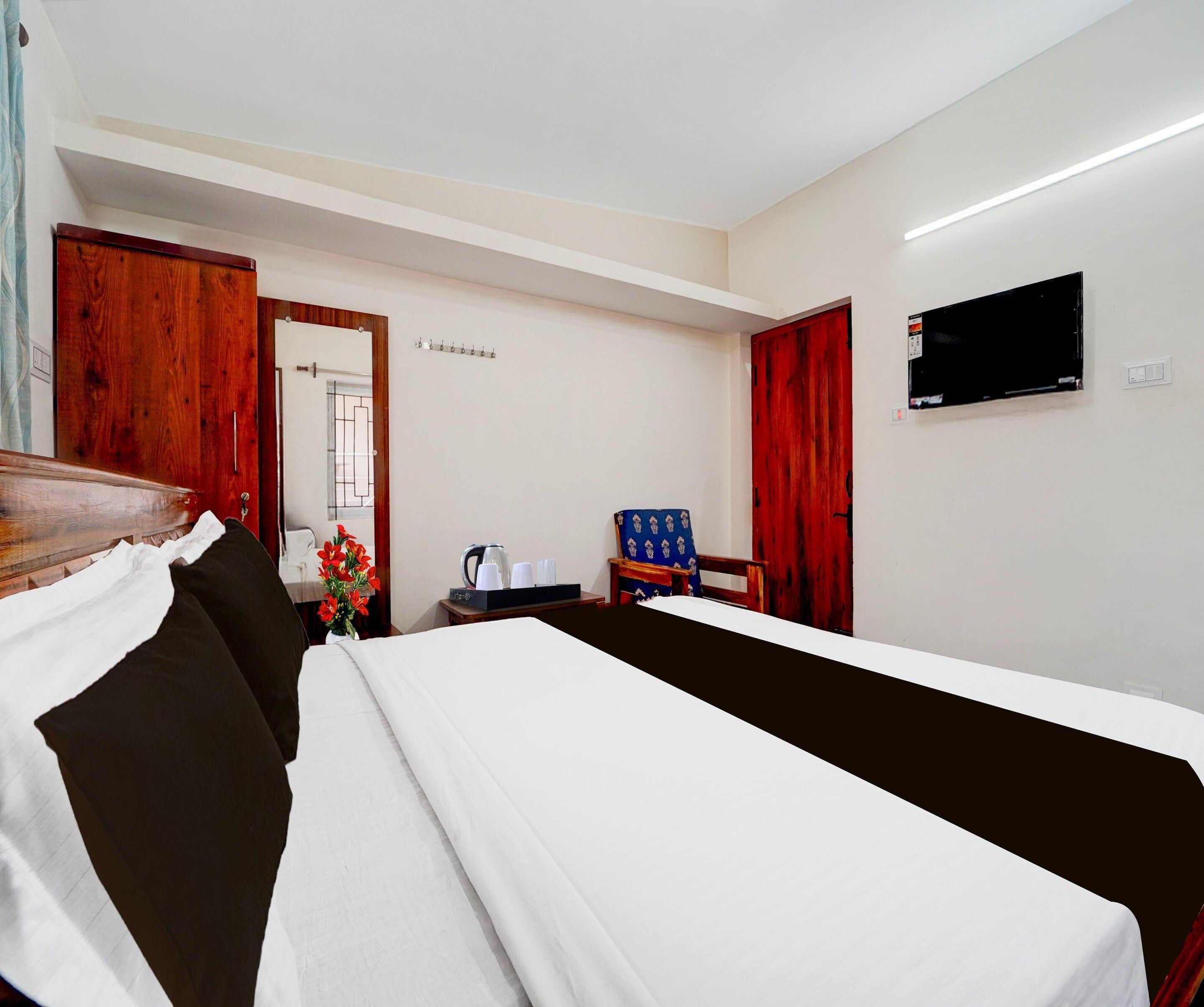 A hotel room with a bed, a desk, a chair, a TV, and a red door.
