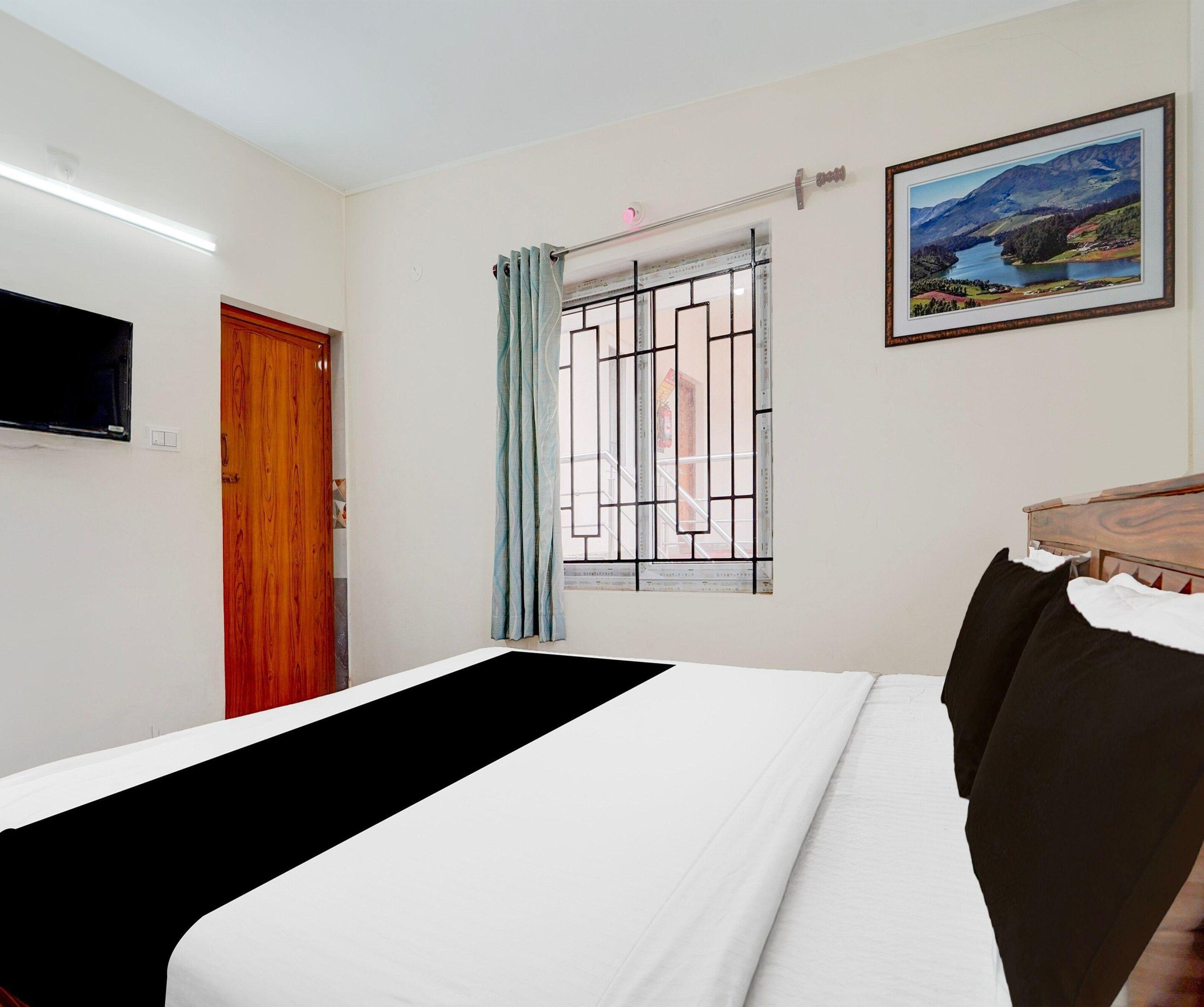 Ein Hotelzimmer mit Bett, Wandfernseher, Fenster mit Vorhang und einem gerahmten Landschaftsbild.