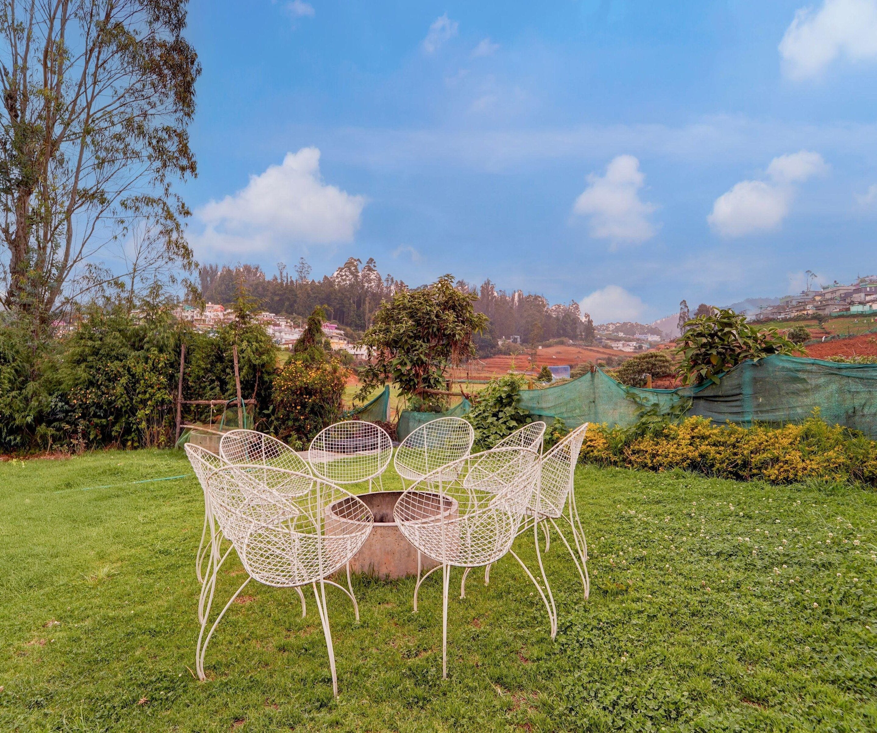 An outdoor seating area with a table and chairs, surrounded by greenery and a view of a hillside village.