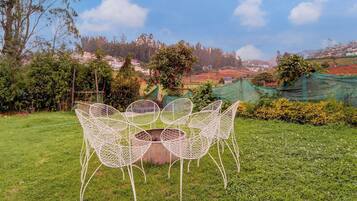 An outdoor seating area with a table and chairs, surrounded by greenery and a view of a hillside village.
