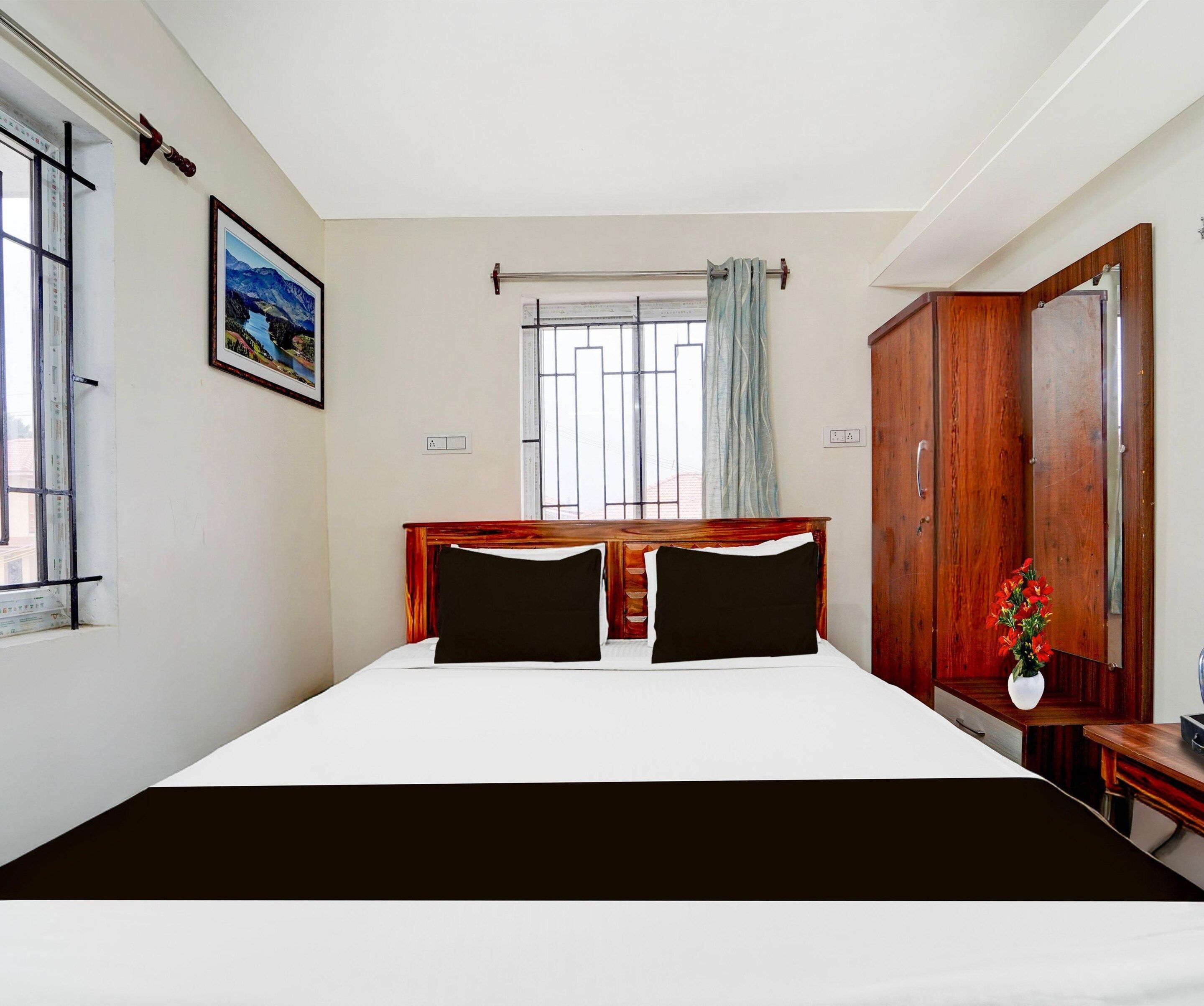 A hotel room with a large bed, a window with bars, a wooden wardrobe, and a painting on the wall.