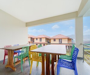 A balcony with a table and colorful chairs, overlooking a row of houses. - Classic Aathira Hill Stay (Ootacamund)