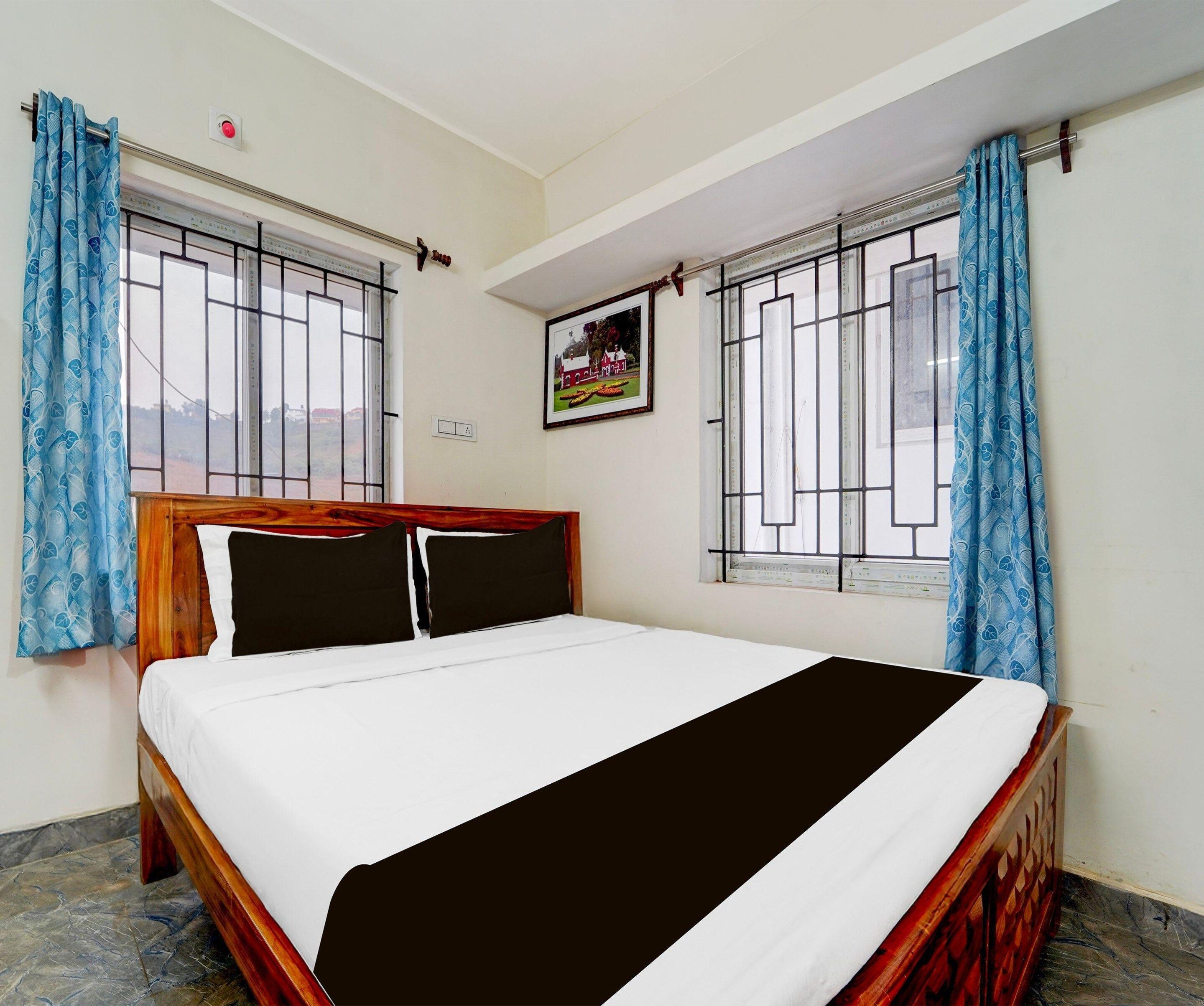 Un dormitorio con cama, cortinas, una ventana con barrotes y un cuadro en la pared.