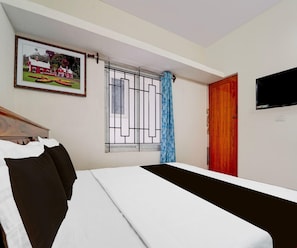A bedroom with a bed, a window with bars, a door, a TV mounted on the wall, and a framed picture on the wall.
