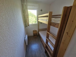 A small, single-bunk room with a window, a radiator, and a wooden bunk bed. - Alpine Ski Apartment in Tignes for 4 (Saint-Sorlin-d'Arves)