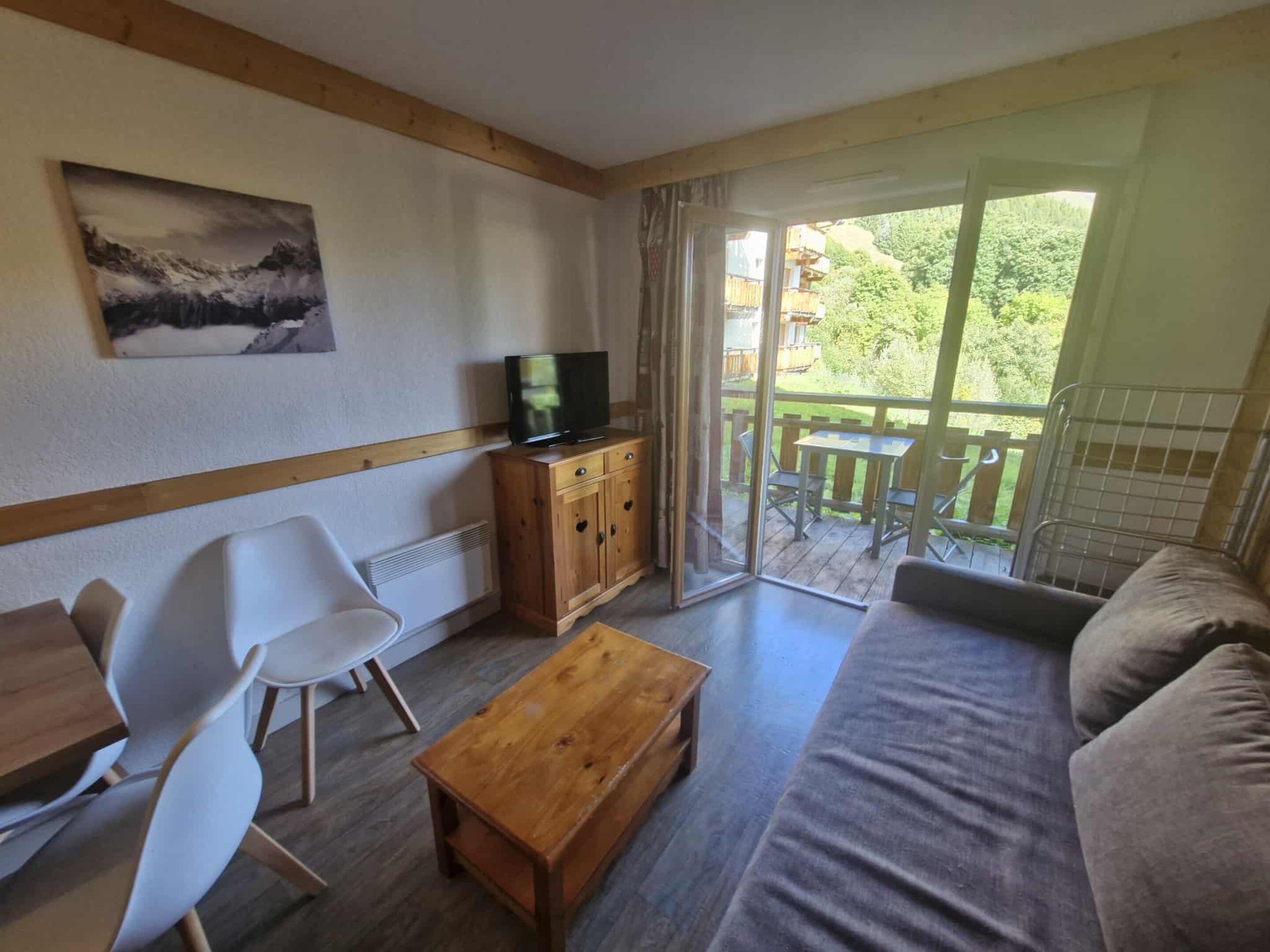 A furnished living room with a sofa, a wooden coffee table, a TV on a cabinet, and a painting on the wall.