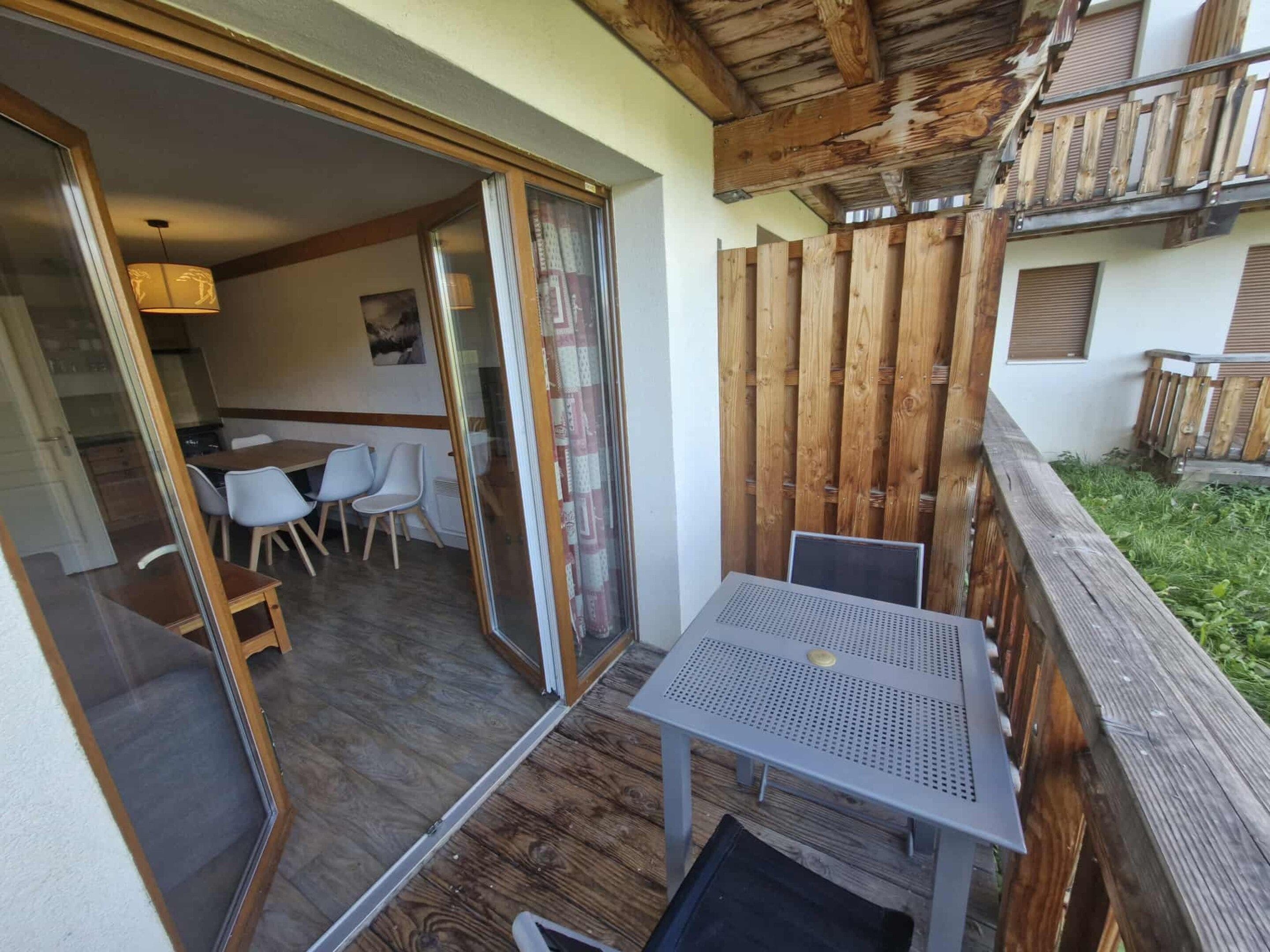 A patio with a table and chairs, a wooden fence, and a building with a balcony.