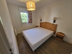 Ein Schlafzimmer mit einem hölzernen Bett, einem Nachttisch, einer Wandlampe und einem Fenster mit Vorhang.