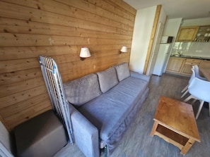 A room with a wooden wall, a grey sofa, a small wooden table, and a white chair. - Alpine Ski Apartment in Tignes for 4 (Saint-Sorlin-d'Arves)