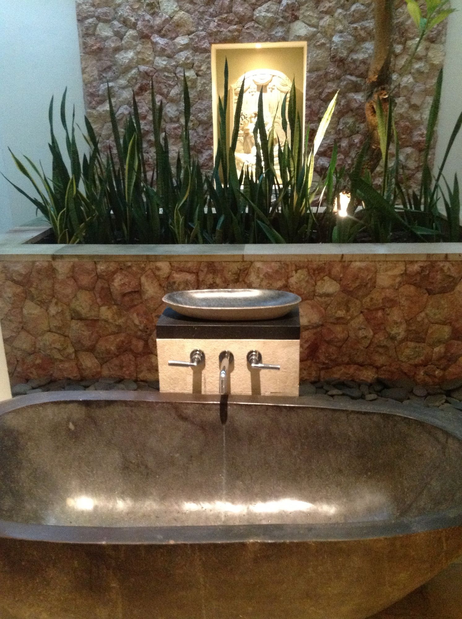 A bathroom with a large, oval-shaped sink, a stone wall, and a small, illuminated wall-mounted light fixture.