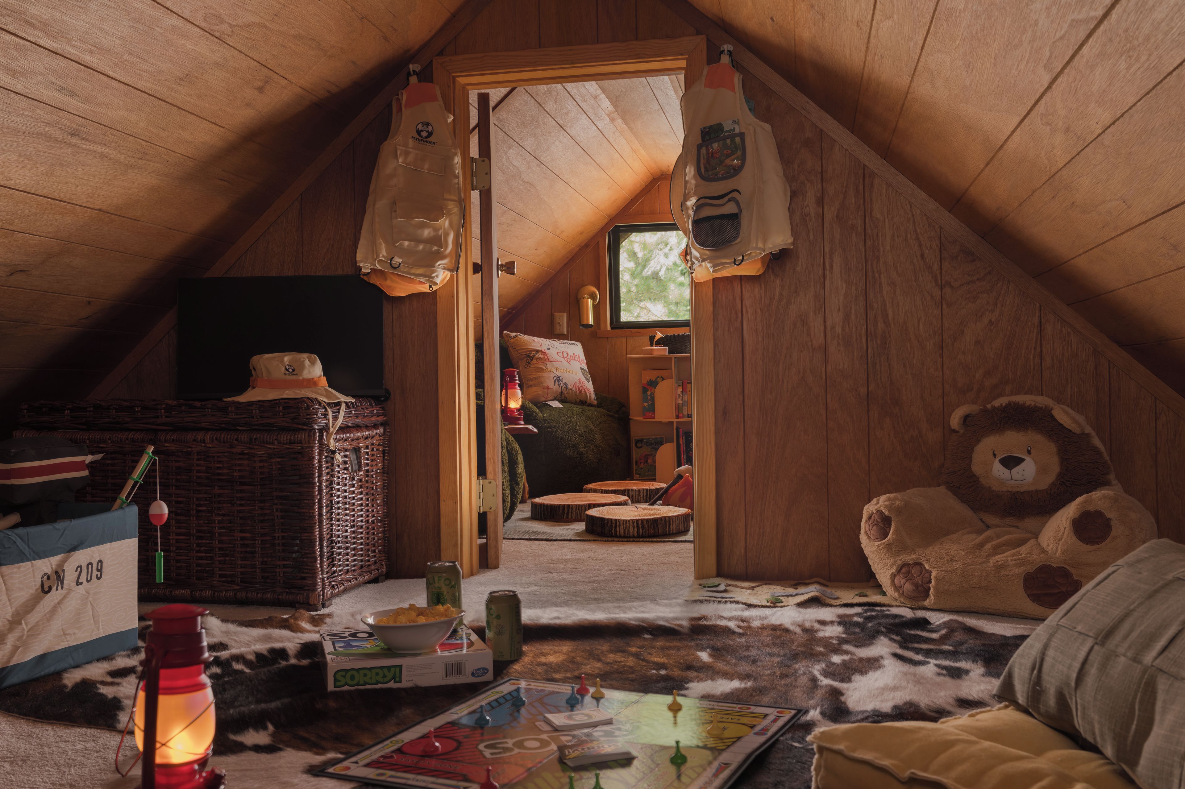 A cozy attic room with a sloped ceiling, a large teddy bear, a wicker basket, and a game board.