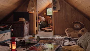 A cozy attic room with a sloped ceiling, a large teddy bear, a wicker basket, and a game board.