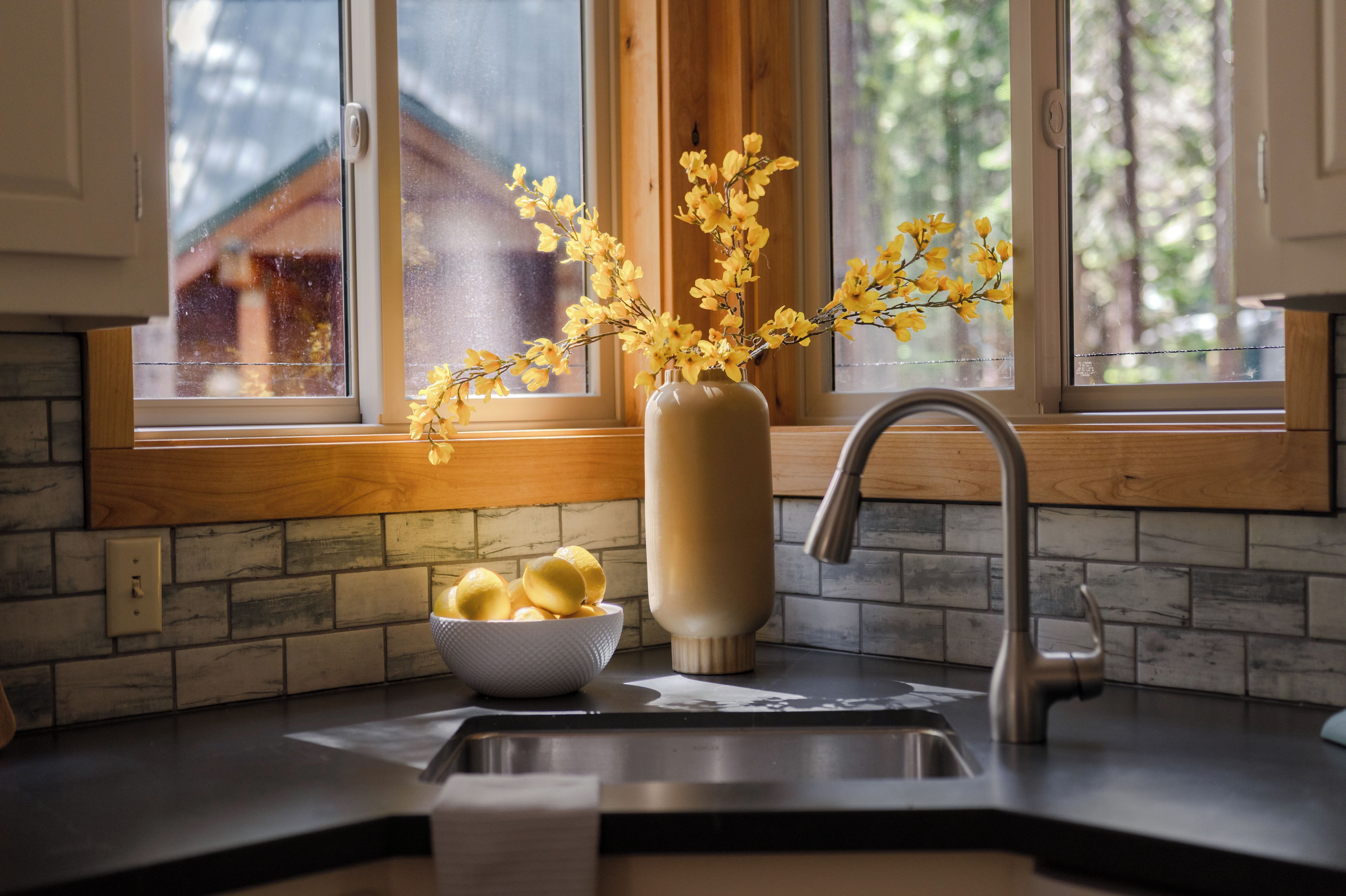 A kitchen with a window, a vase with yellow flowers, and a bowl of lemons.