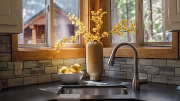 A kitchen with a window, a vase with yellow flowers, and a bowl of lemons.