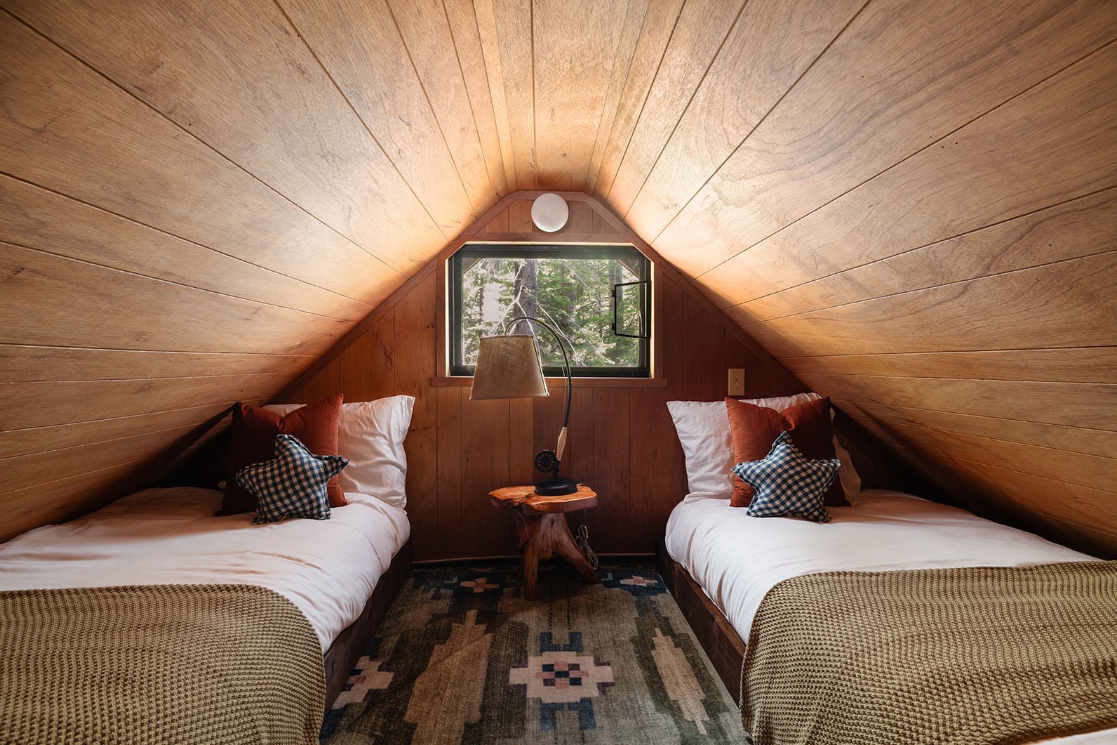 A cozy attic bedroom with two beds, a window, and a lamp.