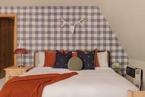 Ein Schlafzimmer mit karierter Wand, einem Bett mit vielen Kissen, einer roten Decke, einer Lampe und einem Heizgerät.