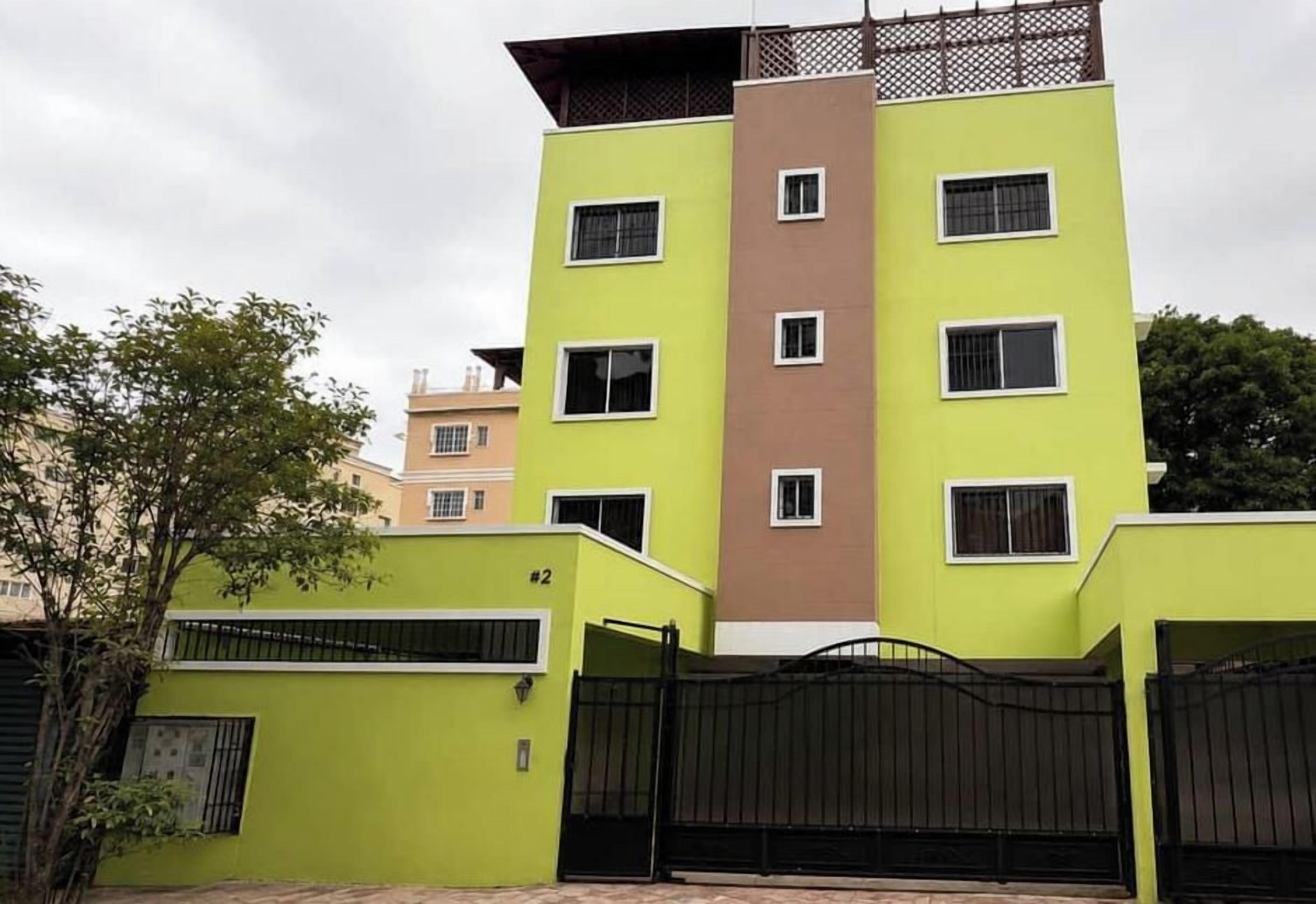 Edificio residencial de varios pisos con techo plano, entrada protegida por una reja y un cartel con el número de la unidad.