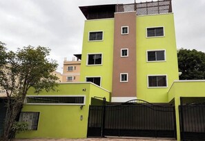 Edificio residencial de varios pisos con techo plano, entrada protegida por una reja y un cartel con el número de la unidad.
