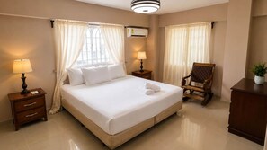 Una habitación de hotel con una cama grande, dos mesitas de noche, una silla y un escritorio.