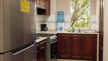 Una cocina con gabinetes de madera, un refrigerador de acero inoxidable, una estufa a gas y un dispensador de agua.