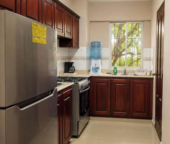 Una cocina con gabinetes de madera, un refrigerador de acero inoxidable, una estufa a gas y un dispensador de agua.