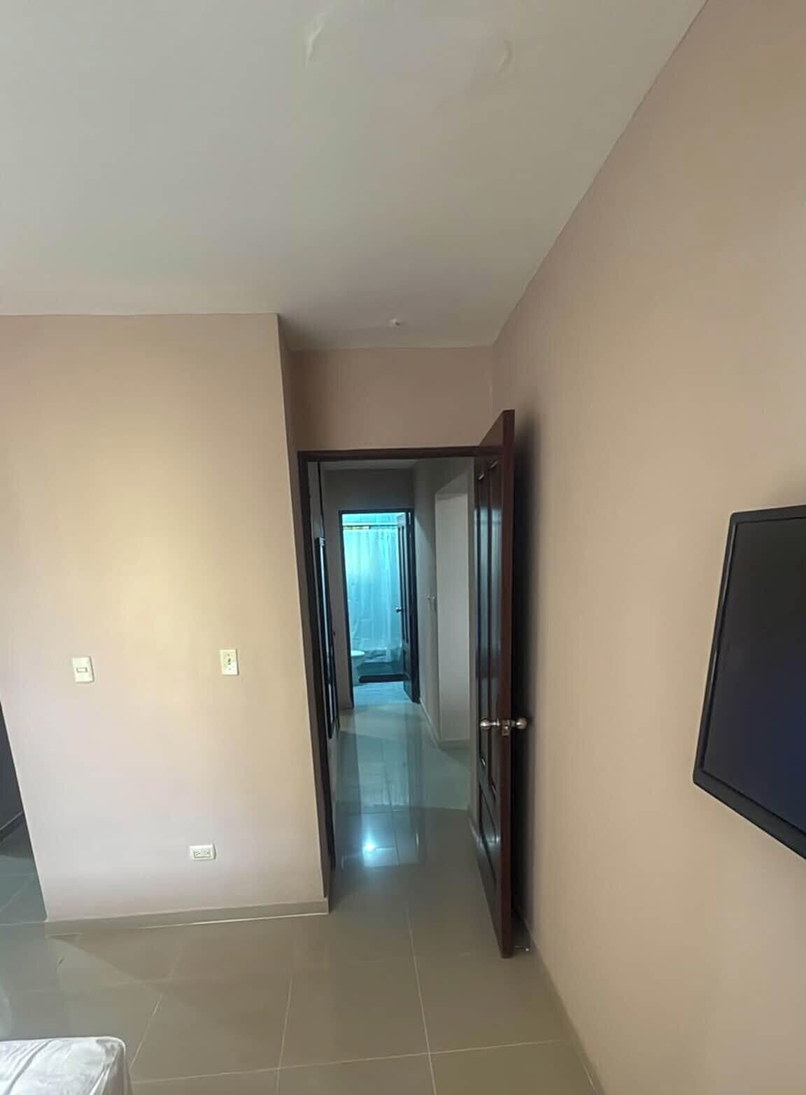 Un pasillo con una puerta que da a una habitación, suelo de baldosas y un televisor fijado a la pared.