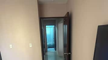 Un pasillo con una puerta que da a una habitación, suelo de baldosas y un televisor fijado a la pared.