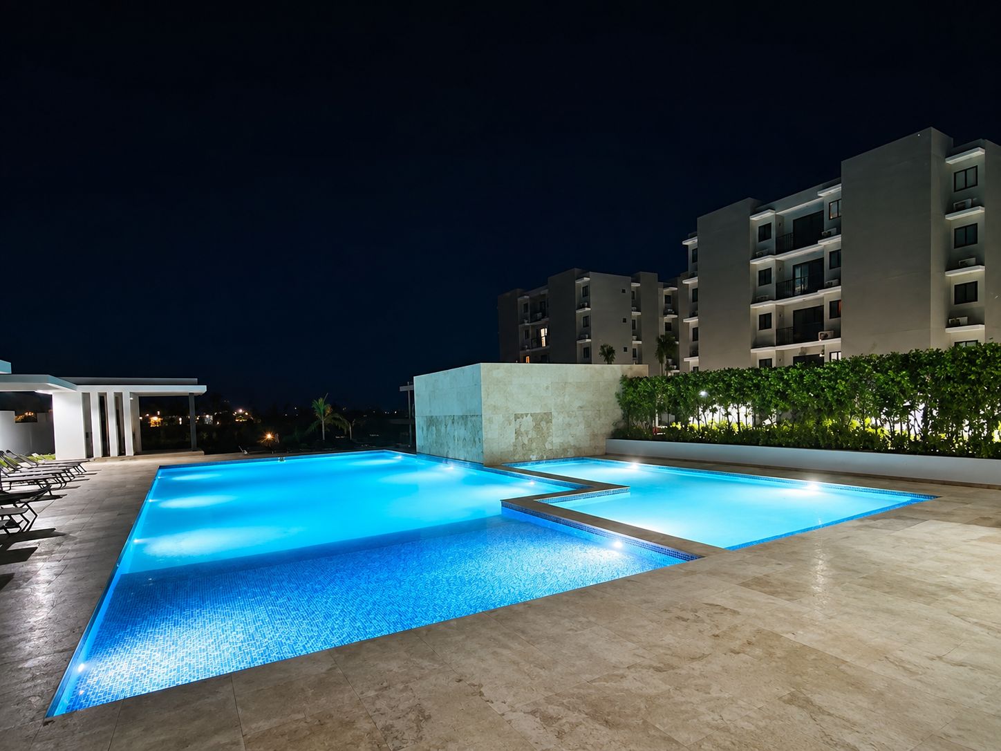 Une piscine dotée d’une terrasse carrelée, entourée d’un petit muret et d’une haie.