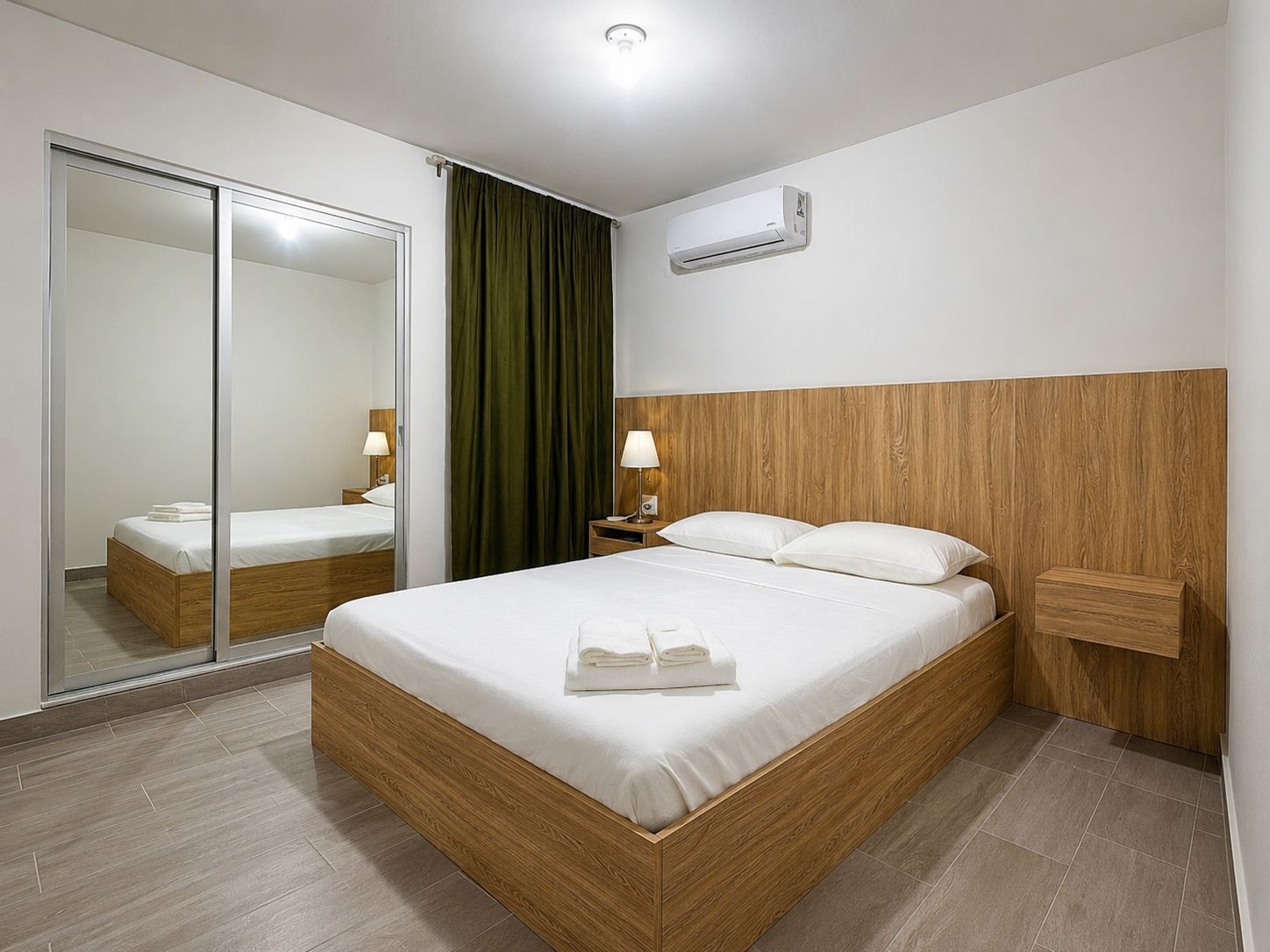 Una habitación de hotel moderna con una cama de madera, un espejo, una cortina verde y un aire acondicionado de pared.