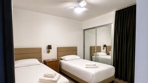 Habitación de hotel con dos camas, ventilador de techo, mesita de noche con lámpara y un espejo grande.