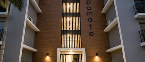 A modern building with a prominent 'Apamate' sign, featuring a central entrance with glass doors and a vertical wooden panel design.