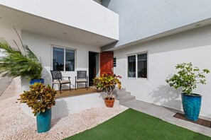 A modern house with a patio, two chairs, a potted plant, and a red door. - Hibisca 2BR Tropical Retreat with Pool & Outdoor Kitchen (Grote Berg)
