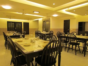 A conference room with multiple tables and chairs, equipped with ceiling fans and recessed lighting. - OYO Premium Ambience Mall 2 (Gurugram)