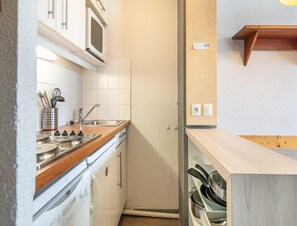 A compact kitchen with white cabinets, a microwave, a sink, and a stove. There is a wooden countertop and a shelf with pots and pans. - Cozy Hideaway With Mountain Vistas (Tignes)